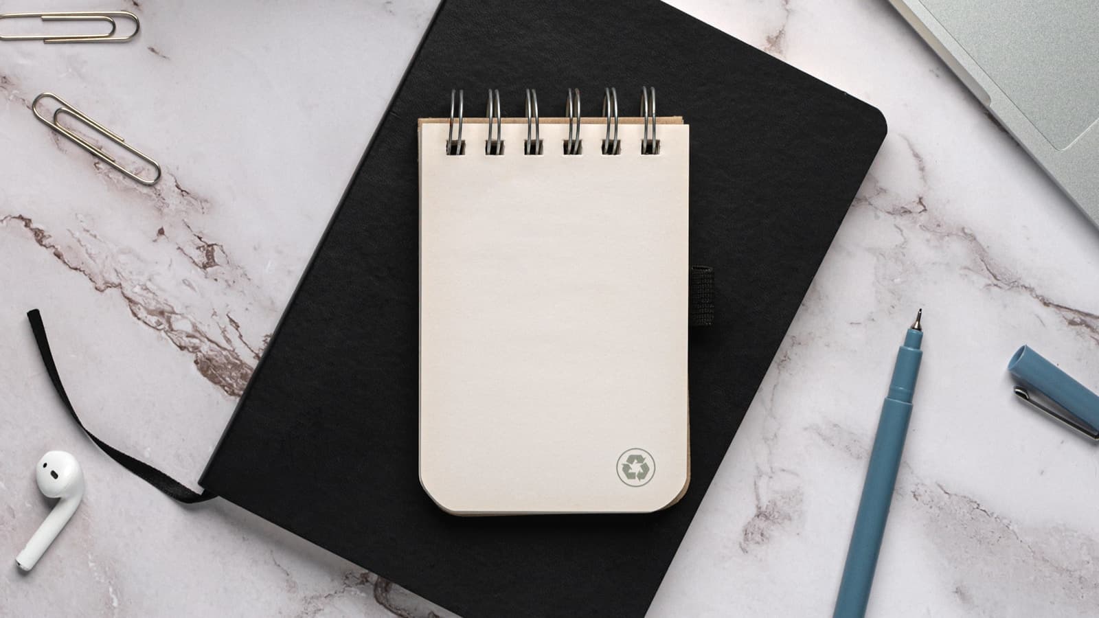 A blank notepad on a black notebook beside a laptop and pen.